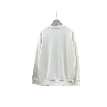 White sweatshirt on a hanger against a gray stone wall with decorative items below.