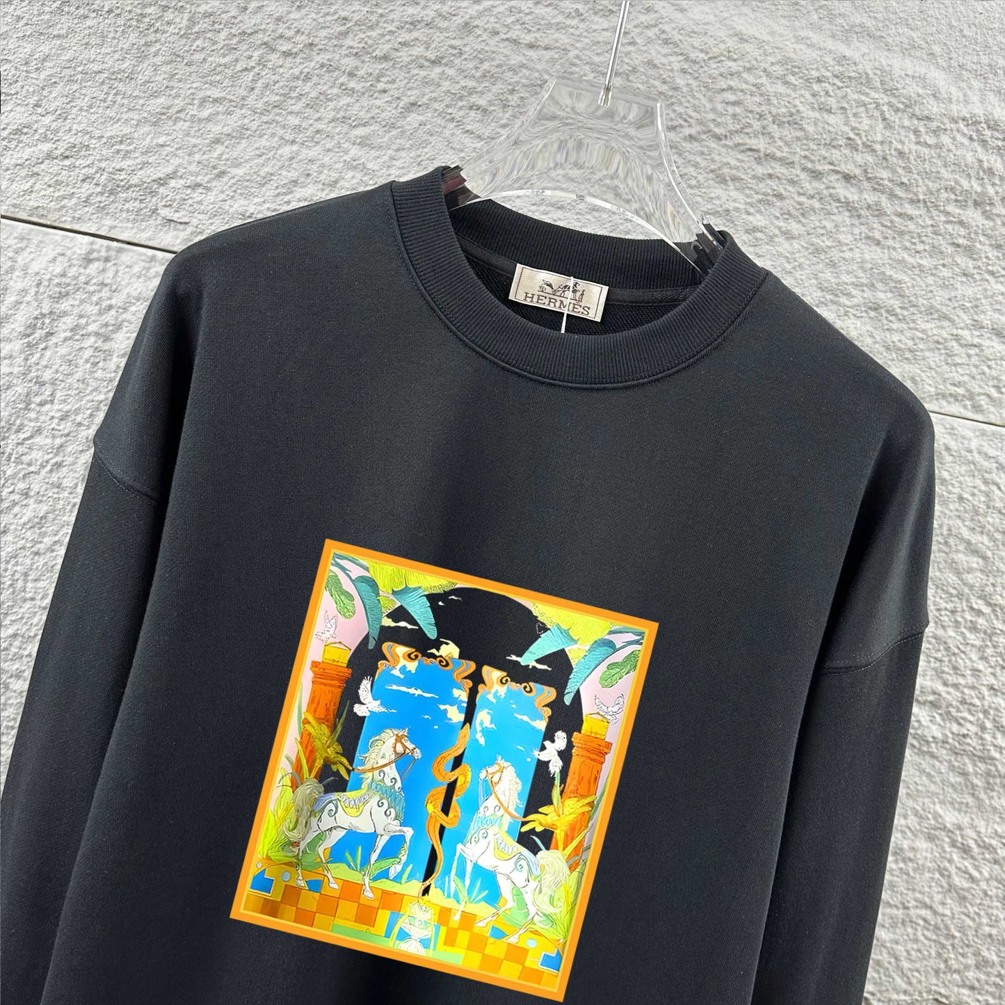 Black sweatshirt with colorful graphic design on a hanger against a light gray wall.