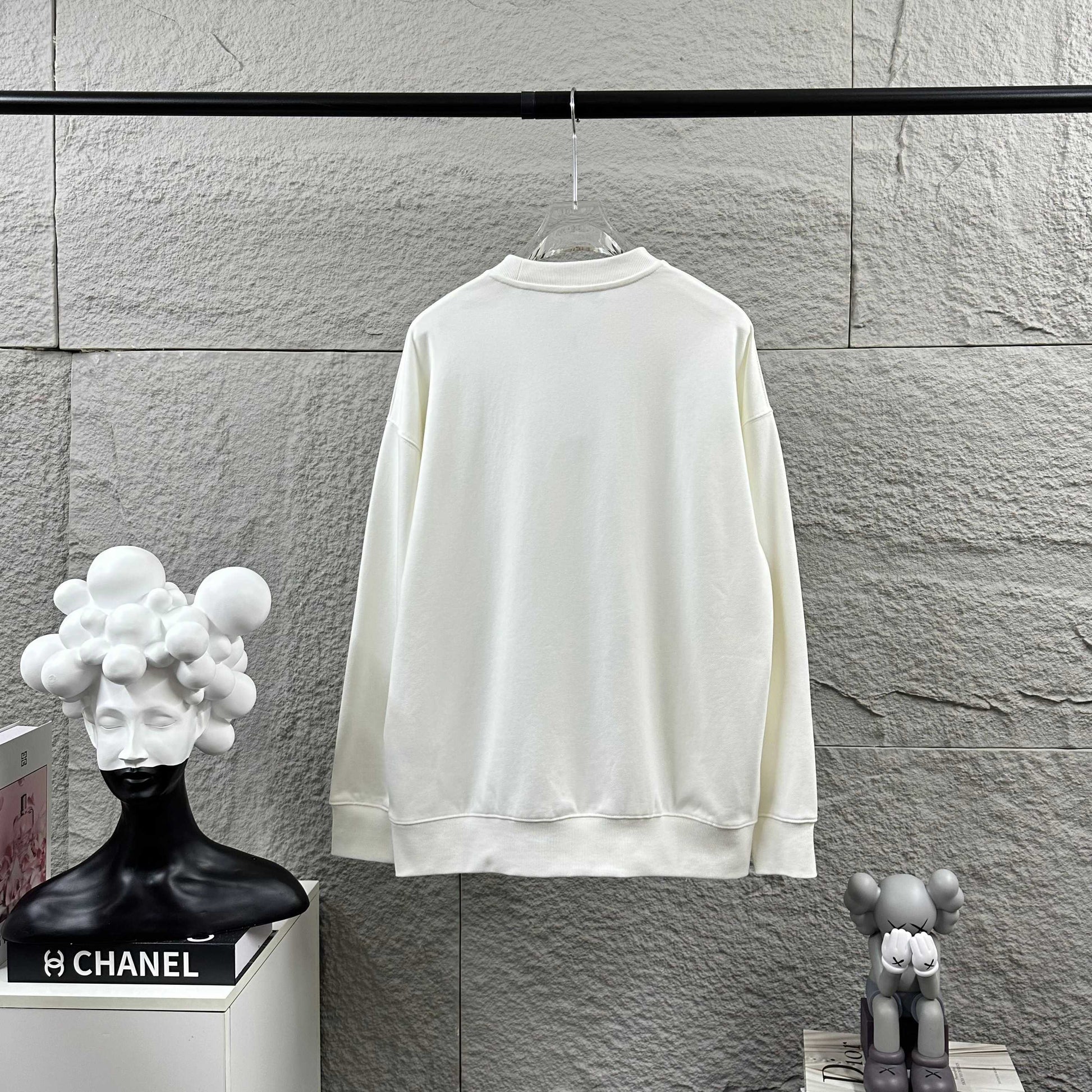 White sweatshirt on a hanger against a gray stone wall with decorative items below.