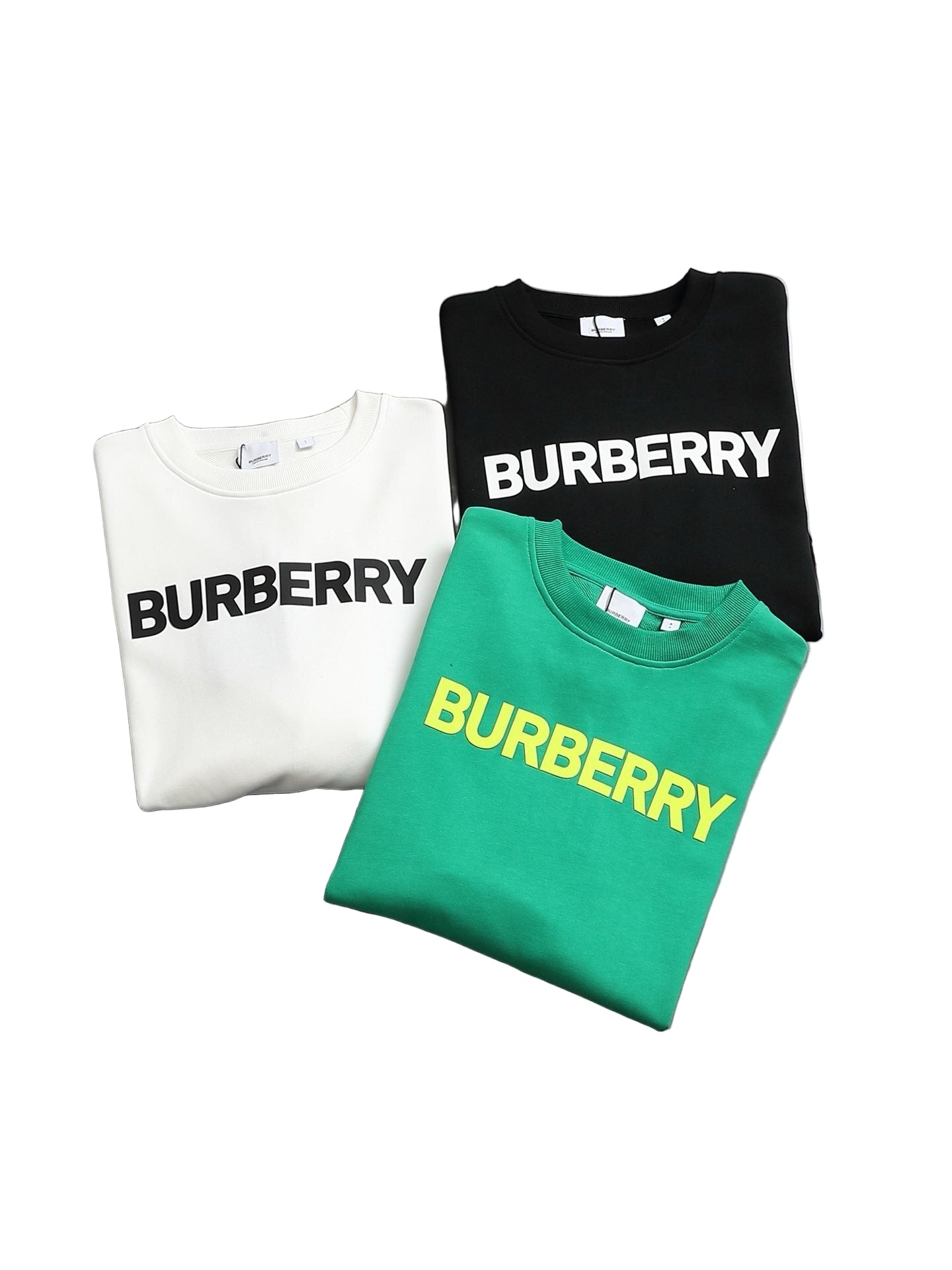 Threesweatshirts in white, black, and green on a gray surface.