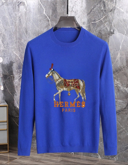 Blue sweater withgraphic on a hanger against a marble wall.