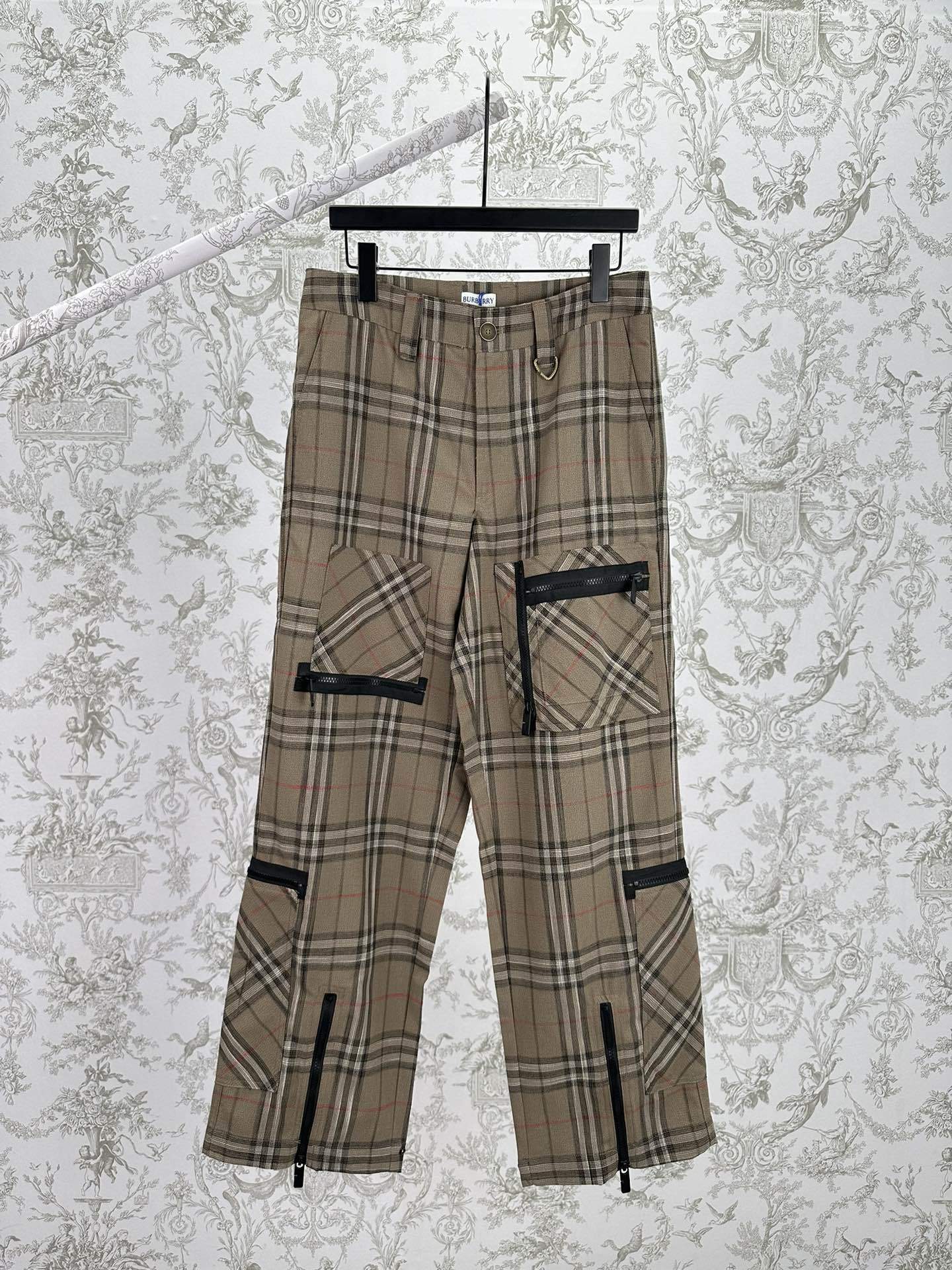 Statement cargo pants featuring an all-over plaid pattern, multiple utility pockets, and zippered accents throughout. Designed with a tapered fit and adjustable ankle zippers for a modern streetwear-inspired look.