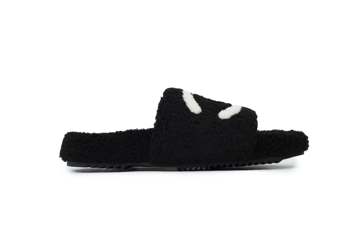 Black fuzzy slide sandal with white accents on a white background
