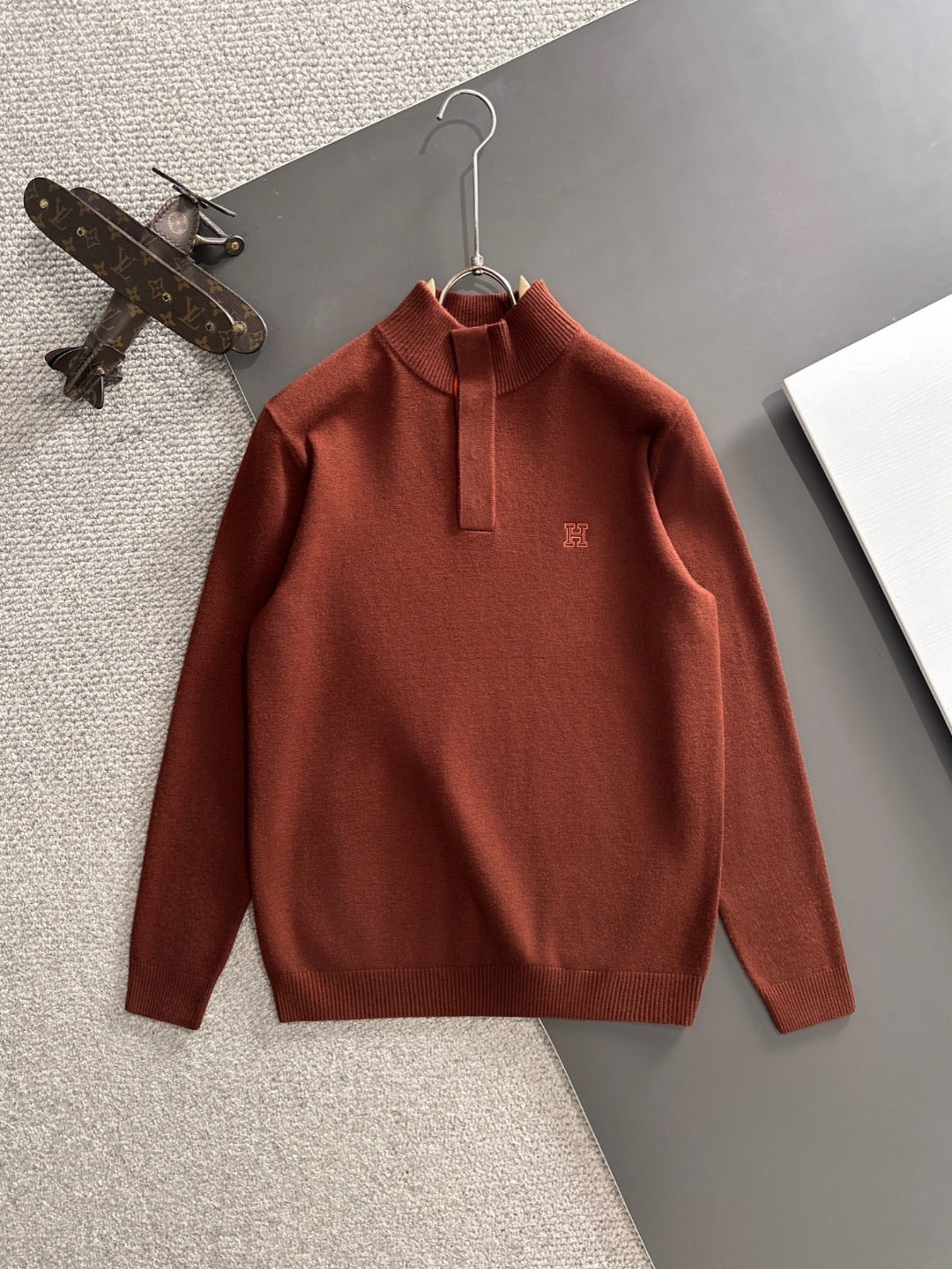 Brown sweater on a hanger with a textured surface and object in the background