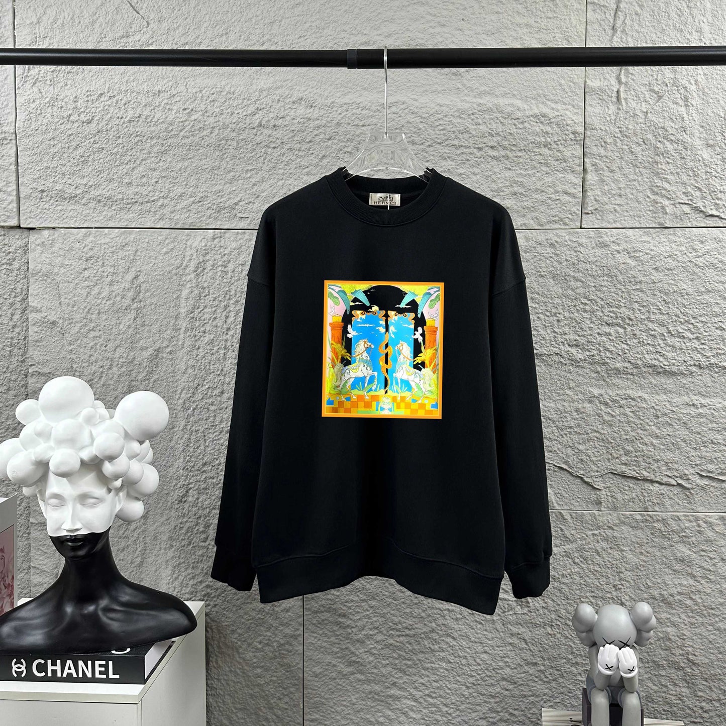 Black sweatshirt with colorful graphic design on a gray wall background