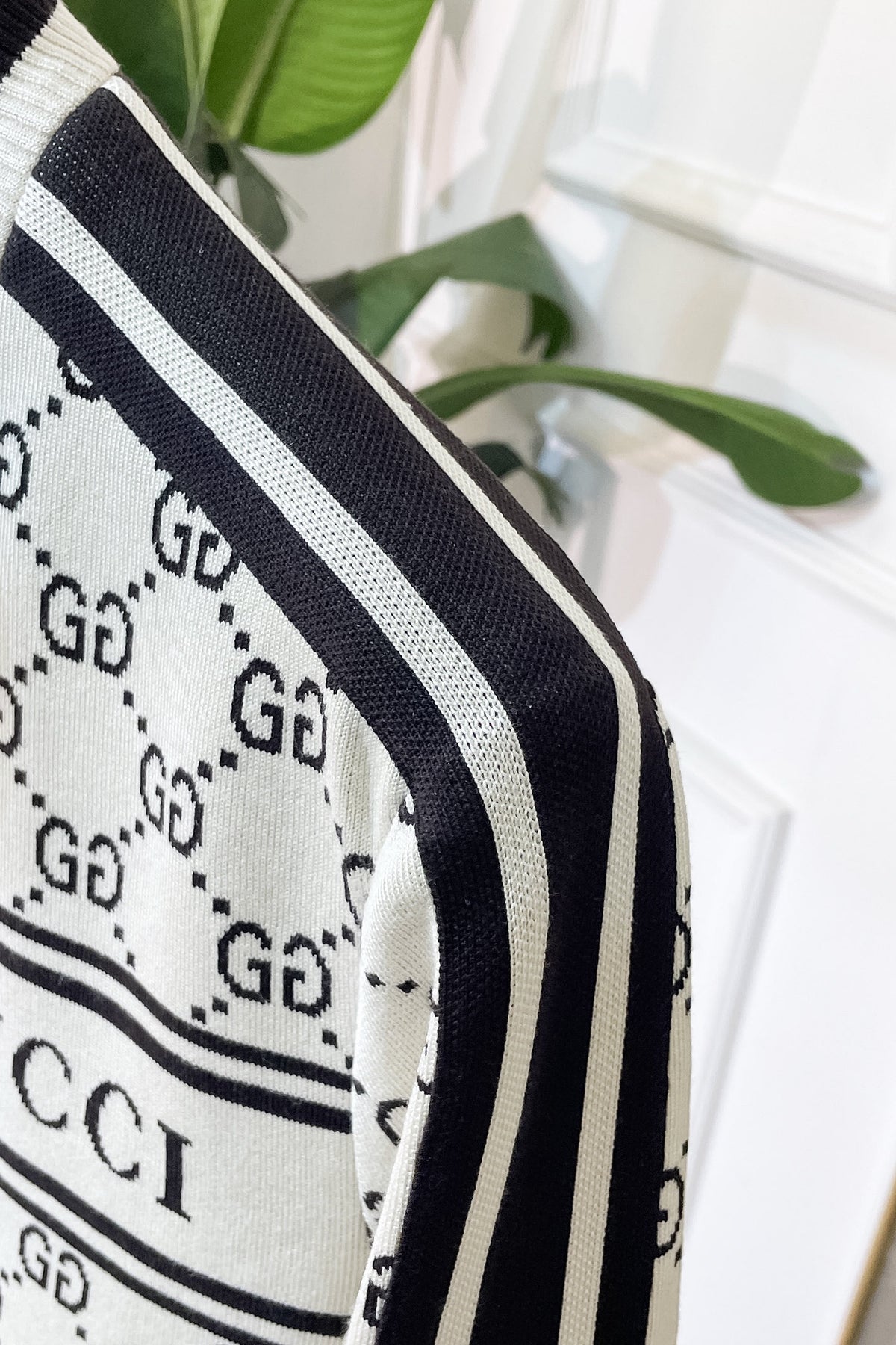 Close-up of aknit sweater featuring the brand's signature GG monogram pattern in black on an off-white background, with black and white stripes along the sleeve.