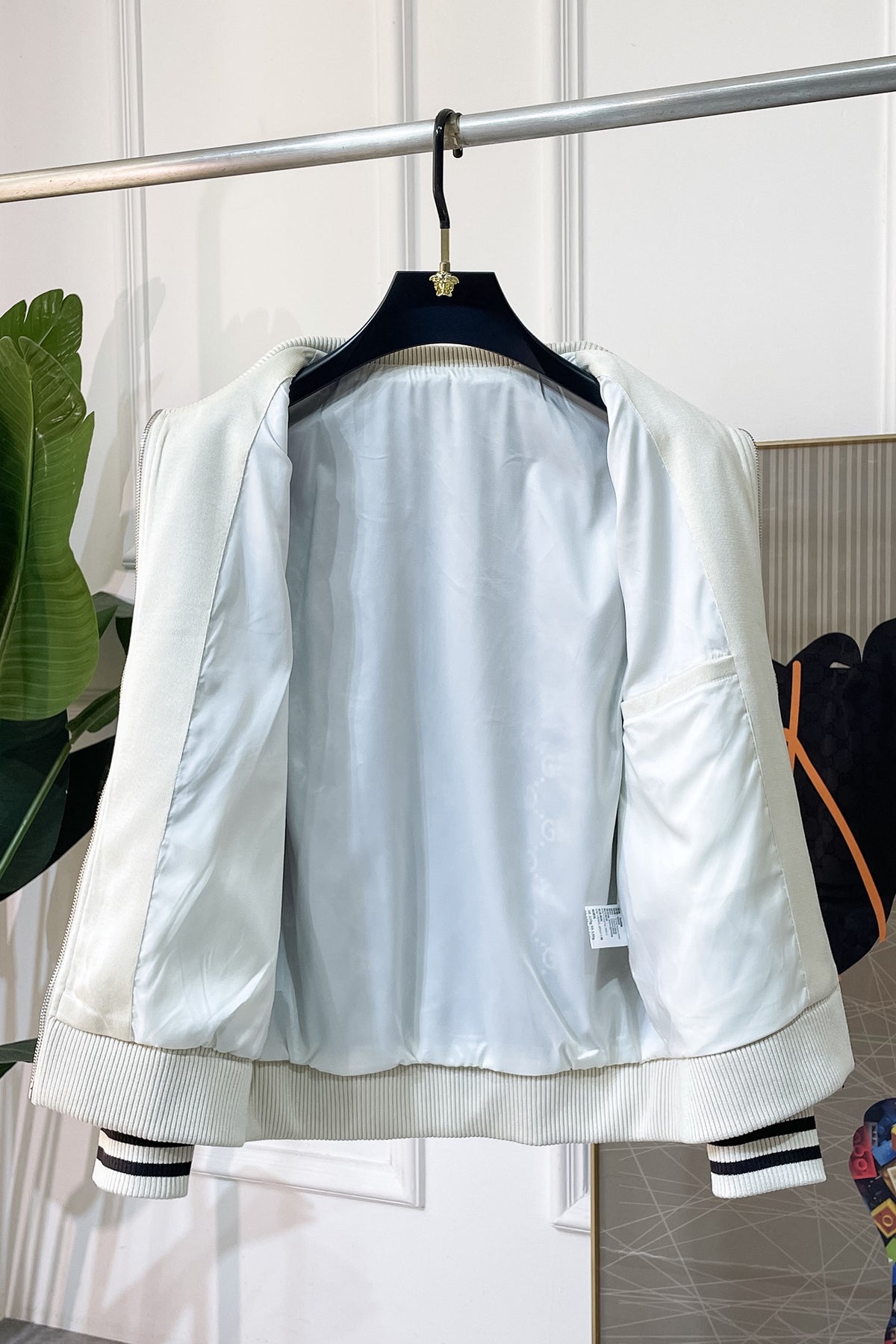 A light-colored satin bomber jacket hanging on a black hanger, showing the interior lining and striped ribbed cuffs and hem.
